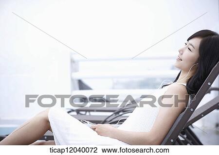 A woman in white dress lying on a sunbed listening to a music View Large Photo Image Stock Image - A woman in white dress lying on a sunbed listening to a music. Fotosearch