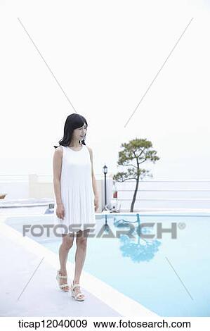 Stock Photo - A woman in white dress next to a pool walking . Fotosearch