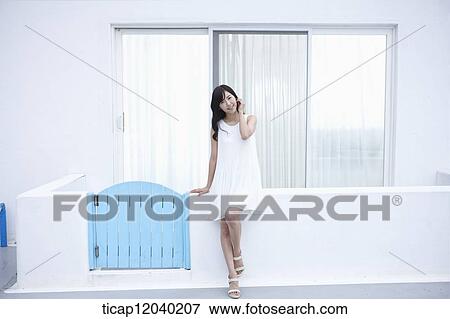 Stock Photo - A woman in white dress posing while sitting on a fence . Fotosearch