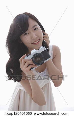 Stock Image - A woman in white dress smiling while holding a retro camera. Fotosearch