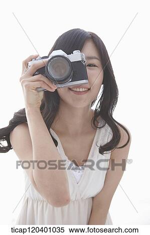 Stock Photography - A woman in white dress taking a picture with a retro camera. Fotosearch