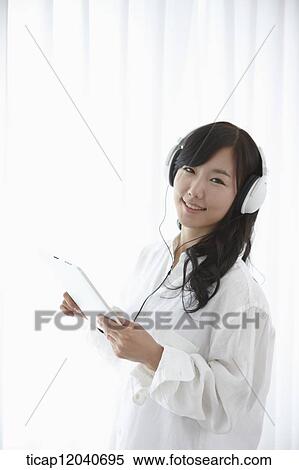 A woman in white shirt and white headphone listening to a music with a tablet View Large Photo Image Stock Photography - A woman in white shirt and white headphone listening to a music with a tablet. Fotosearch