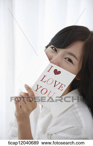 Stock Photo - A woman in white shirt covering her mouth with a book while smiling. Fotosearch