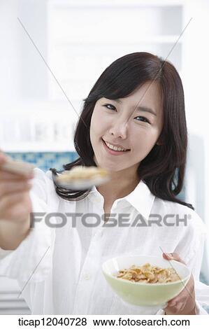 A woman in white shirt handing a spoon of cereal from a bowl of cereal in a kitchen View Large Photo Image Stock Photo - A woman in white shirt handing a spoon of cereal from a bowl of cereal in a kitchen. Fotosearch