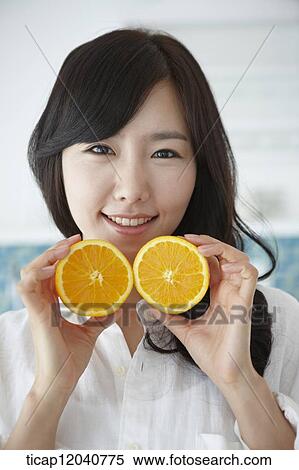 A woman in white shirt holding two oranges in a kitchen View Large Photo Image Stock Photography - A woman in white shirt holding two oranges in a kitchen. Fotosearch