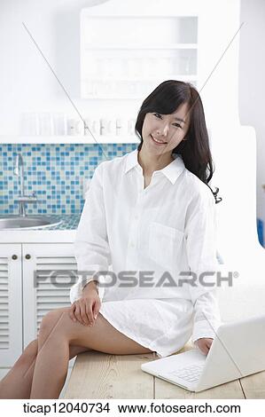 A woman in white shirt sitting on a table using her laptop View Large Photo Image Picture - A woman in white shirt sitting on a table using her laptop. Fotosearch