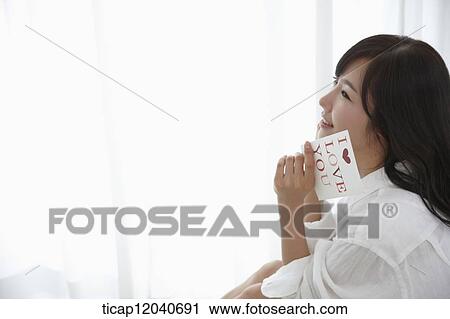 Stock Image - A woman in white shirt smiling while holding a book. Fotosearch