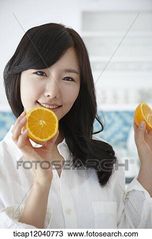 A woman in white shirt smiling while holding oranges in a kitchen View Large Photo Image Stock Image - A woman in white shirt smiling while holding oranges in a kitchen. Fotosearch