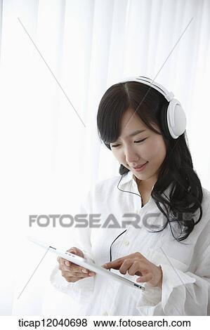 Stock Photo - A woman in white shirt wearing a headphone touching her a tablet. Fotosearch