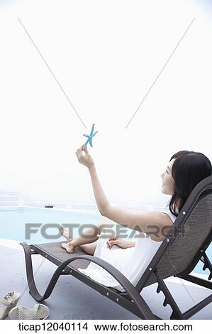 A woman looking at a starfish in her hand while sitting on a sunbed View Large Photo Image Picture - A woman looking at a starfish in her hand while sitting on a sunbed. Fotosearch