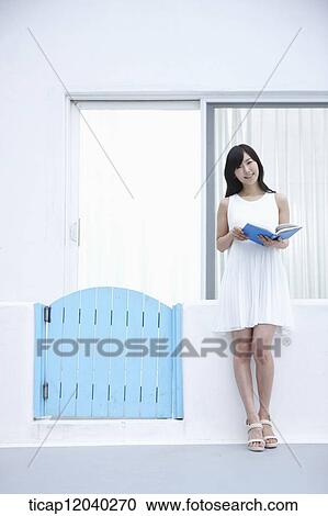 A woman reading a book leaning on a white fence View Large Photo Image Stock Image - A woman reading a book leaning on a white fence. Fotosearch