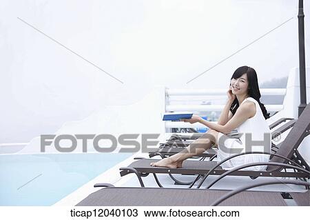 A woman smiling while holding a book on a sunbed View Large Photo Image Stock Image - A woman smiling while holding a book on a sunbed. Fotosearch