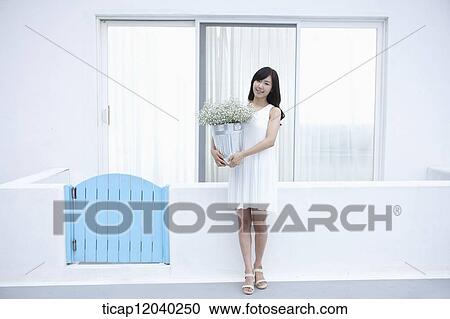 Stock Image - A woman standing with a bunch of flower in front of a white fence. Fotosearch