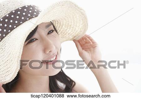Stock Photo - A woman wearing a beach hat smiling while touching her hat. Fotosearch