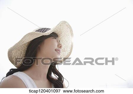 Stock Photo - A woman wearing a white dress and straw hat smiling in white background. Fotosearch