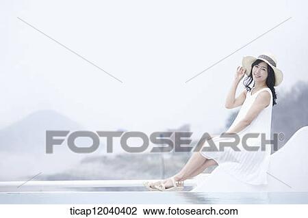 A woman with a white dress and a sun hat sitting next to a swimming pool while looking at the camera View Large Photo Image Stock Image - A woman with a white dress and a sun hat sitting next to a swimming pool while looking at the camera. Fotosearch