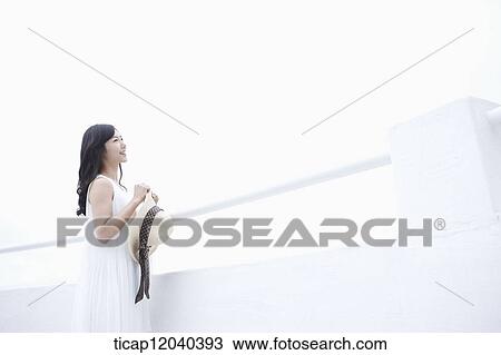 A woman with a white dress standing next to a white fance with a sun hat in her hands while looking at the view View Large Photo Image Stock Image - A woman with a white dress standing next to a white fance with a sun hat in her hands while looking at the view. Fotosearch
