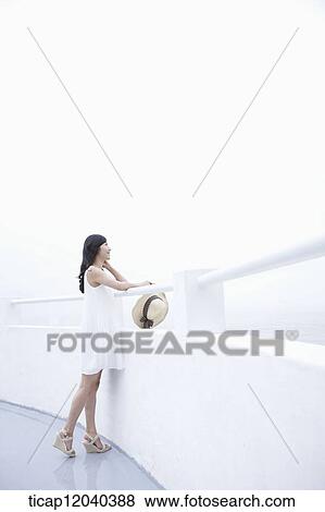 A woman with a white dress standing next to a white fance with a sun hat in her hand View Large Photo Image Stock Photo - A woman with a white dress standing next to a white fance with a sun hat in her hand. Fotosearch