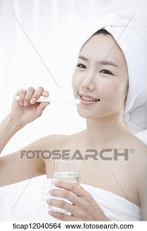 Picture - A woman with bath towel around body and over head putting brushing her teeth. Fotosearch
