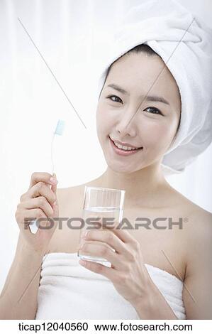 Stock Image - A woman with bath towel around body and over head putting brushing her teeth. Fotosearch