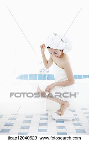 A woman with bath towel around her body and over head weighing herself in a bathroom View Large Photo Image Stock Image - A woman with bath towel around her body and over head weighing herself in a bathroom. Fotosearch