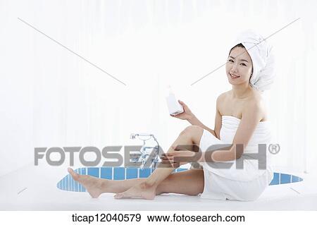 A woman with bath towel around her body and over head sitting at edge of bath tub putting lotion on her leg View Large Photo Image Stock Photo - A woman with bath towel around her body and over head sitting at edge of bath tub putting lotion on her leg. Fotosearch