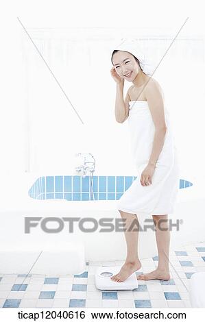 A woman with bath towel around her body and over head weighing herself on a scale while smiling at camera View Large Photo Image Stock Photograph - A woman with bath towel around her body and over head weighing herself on a scale while smiling at camera. Fotosearch