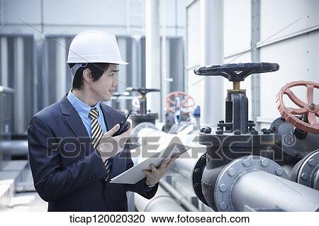 Stock Image - An architect holding a report standing next to a pipeline valve. Fotosearch