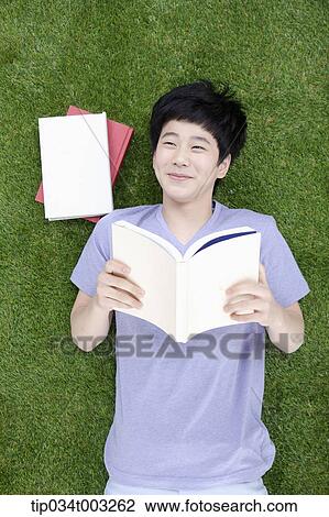 Stock Image - boy lying on the ground and holding a book. Fotosearch