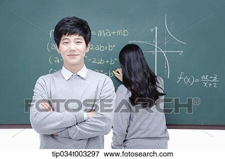 Stock Photo - boy standing with his arms folded and girl solving a problem on the blackboard . Fotosearch