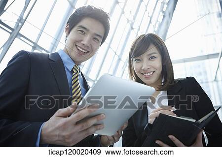 Stock Photo - Businessman and woman smiling while holding a report and schedule book. Fotosearch
