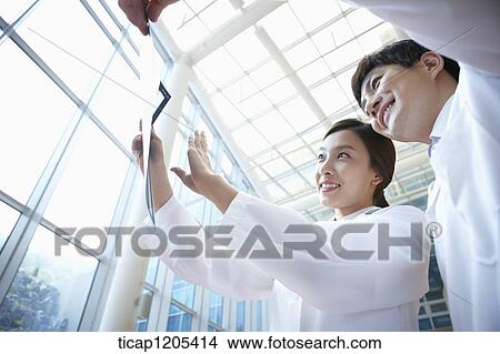Doctors in a white dressing gown happily talking about a x-ray picture View Large Photo Image Picture - Doctors in a white dressing gown happily talking about a x-ray picture . Fotosearch