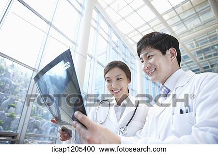 Doctors in a white dressing gown looking at x-ray picture happily View Large Photo Image Stock Image - Doctors in a white dressing gown looking at x-ray picture happily. Fotosearch