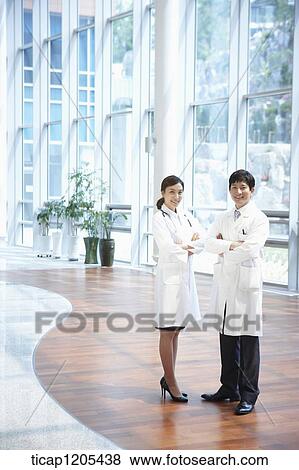 Stock Photo - Doctors in a white dressing gown standing in a nice building with their arms crossed. Fotosearch