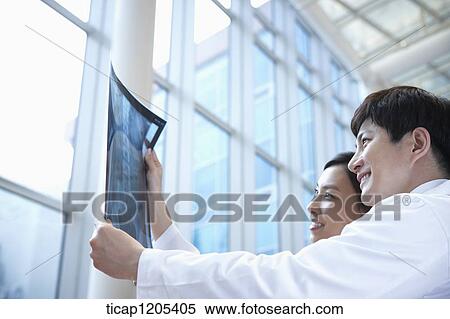 Stock Photography - Doctors in a white dressing gown looking at x-ray picture happily. Fotosearch