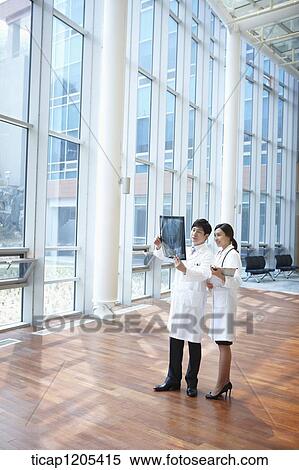 Doctors in a white dressing gown happily talking about a x-ray picture in a building View Large Photo Image Stock Photography - Doctors in a white dressing gown happily talking about a x-ray picture in a building. Fotosearch