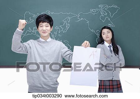 Stock Image - girl leaning against the blackboard and boy holding a paper. Fotosearch