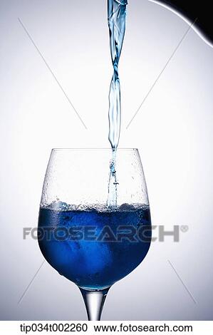 Stock Image - glass being filled with blue water. Fotosearch