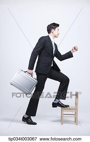 Stock Photo - man carrying a briefcase and stepping up the wooden chair . Fotosearch