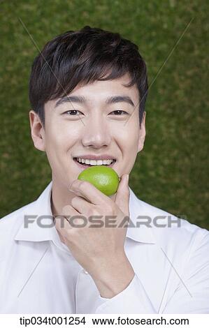 Picture - man eating green citrus. Fotosearch