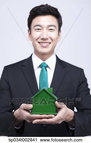Stock Image - man holding a green house model on his hands. Fotosearch