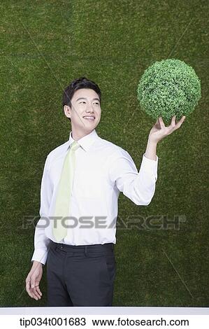 Stock Image - man holding a sphere covered with grass. Fotosearch