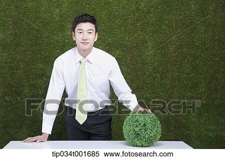 Stock Photography - man holding a sphere covered with grass. Fotosearch
