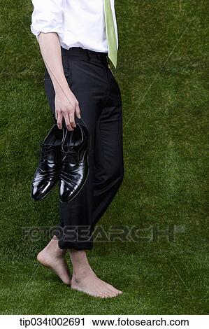 Stock Image - man holding his shoes in his bare feet. Fotosearch