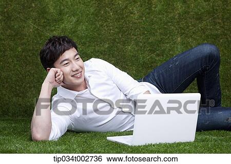 Stock Photograph - man lying on his side and using a laptop . Fotosearch
