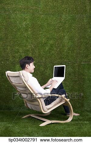 Stock Image - man sitting on the armchair and using laptop. Fotosearch