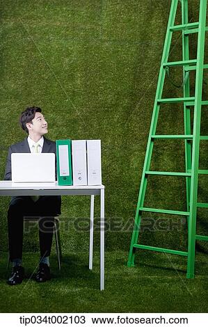 Stock Image - man sitting on the desk and looking at the ladder . Fotosearch