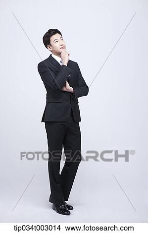 Picture - man standing and resting his chin on his hand . Fotosearch