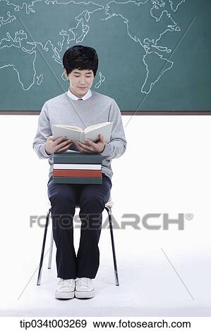 Stock Photo - schoolboy putting a stack of books on his knees and reading a book. Fotosearch