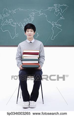 Stock Photography - schoolboy putting a stack of books on his knees. Fotosearch